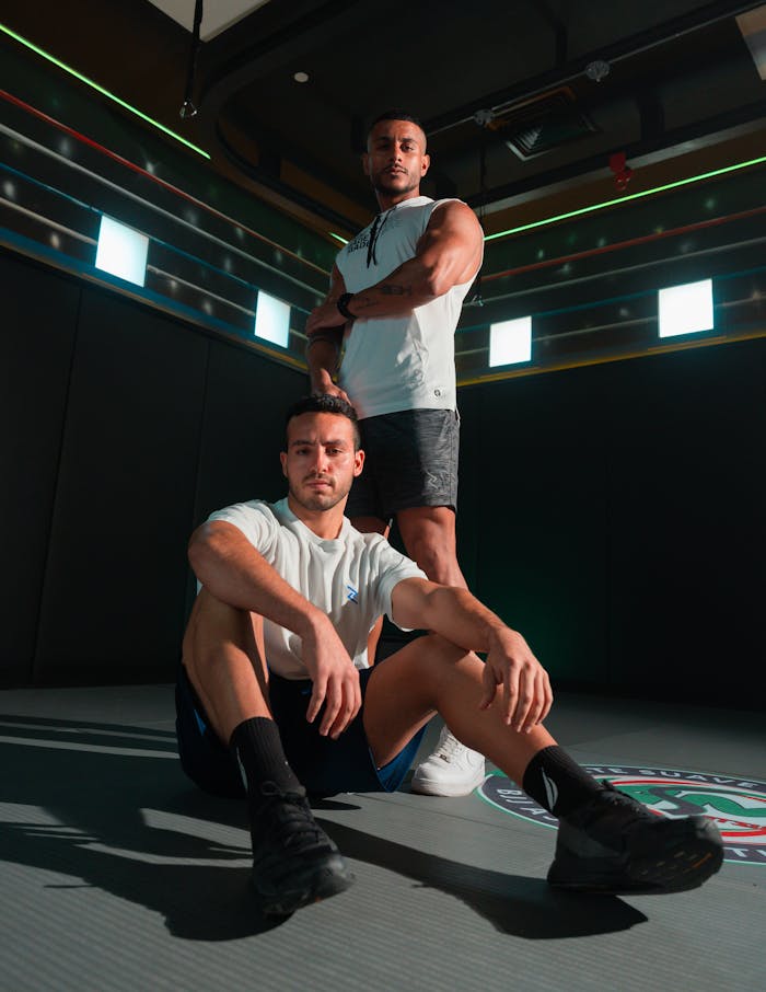 Two athletic men pose confidently in a modern indoor gym environment.