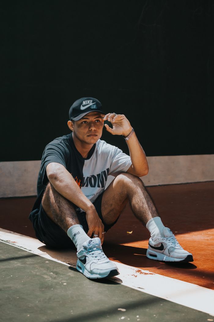 A young male athlete in sportswear sitting on an indoor court in a relaxed pose.